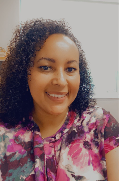 A woman with curly hair and pink shirt smiling.